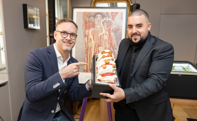 Raimund Saam links und Miloš Zivojinović rechts präsentieren gemeinsam ein Dessert vor einer Klimt-Reproduktion.