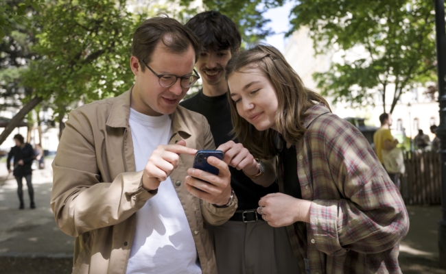 Drei Mitglieder des Politiktrafik-Teams betrachten gemeinsam ein Smartphone im Freien