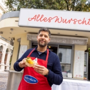 Sebastian Neuschler hält einen Nacho Dog vor seinem Würstelstand „Alles Wurscht“ am Wiener Börseplatz.
