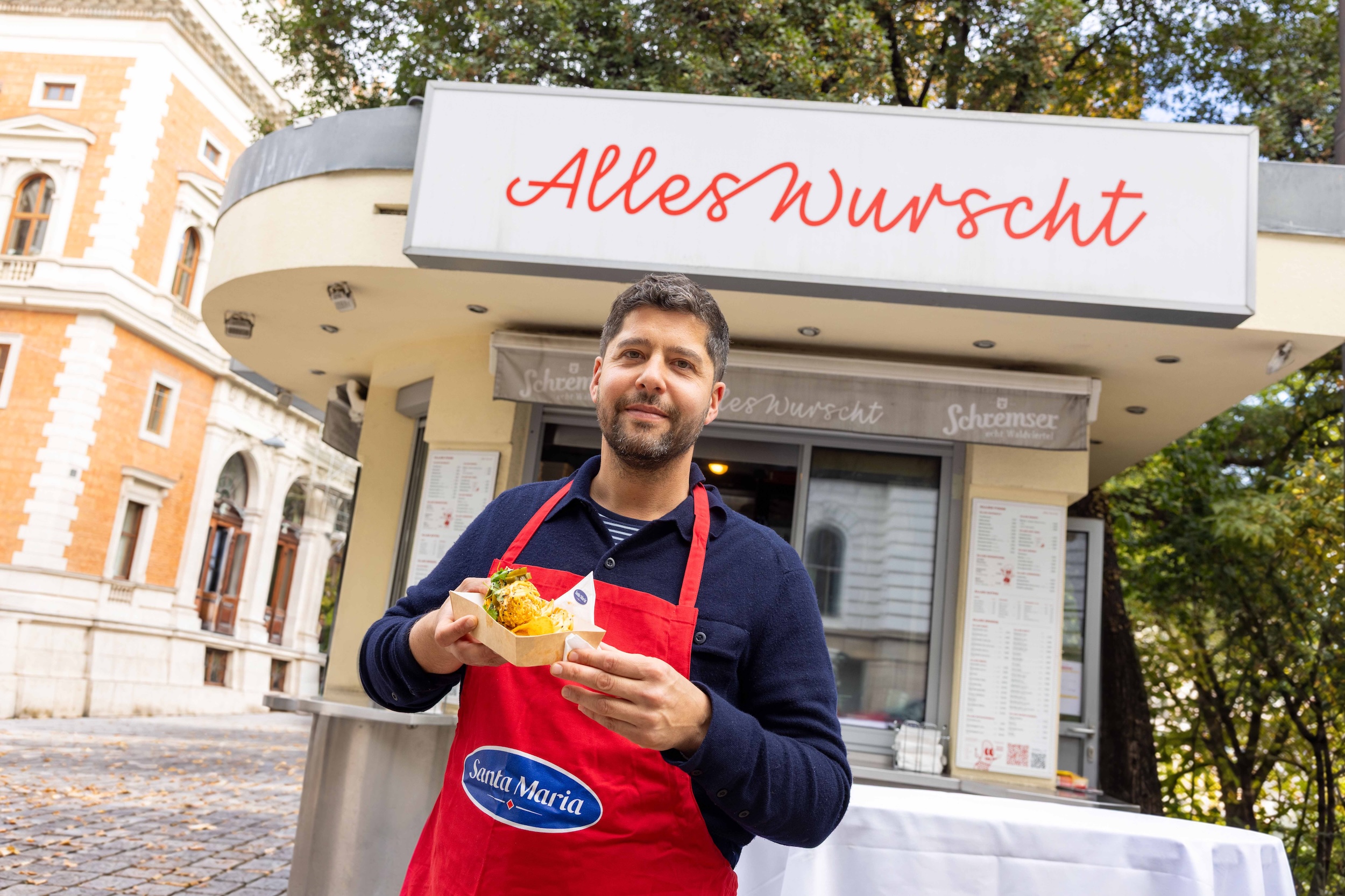 Sebastian Neuschler hält einen Nacho Dog vor seinem Würstelstand „Alles Wurscht“ am Wiener Börseplatz.