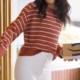 Eine Person im gestreiften Pullover steht mit einem Amazon-Paket an einer geöffneten Haustür.