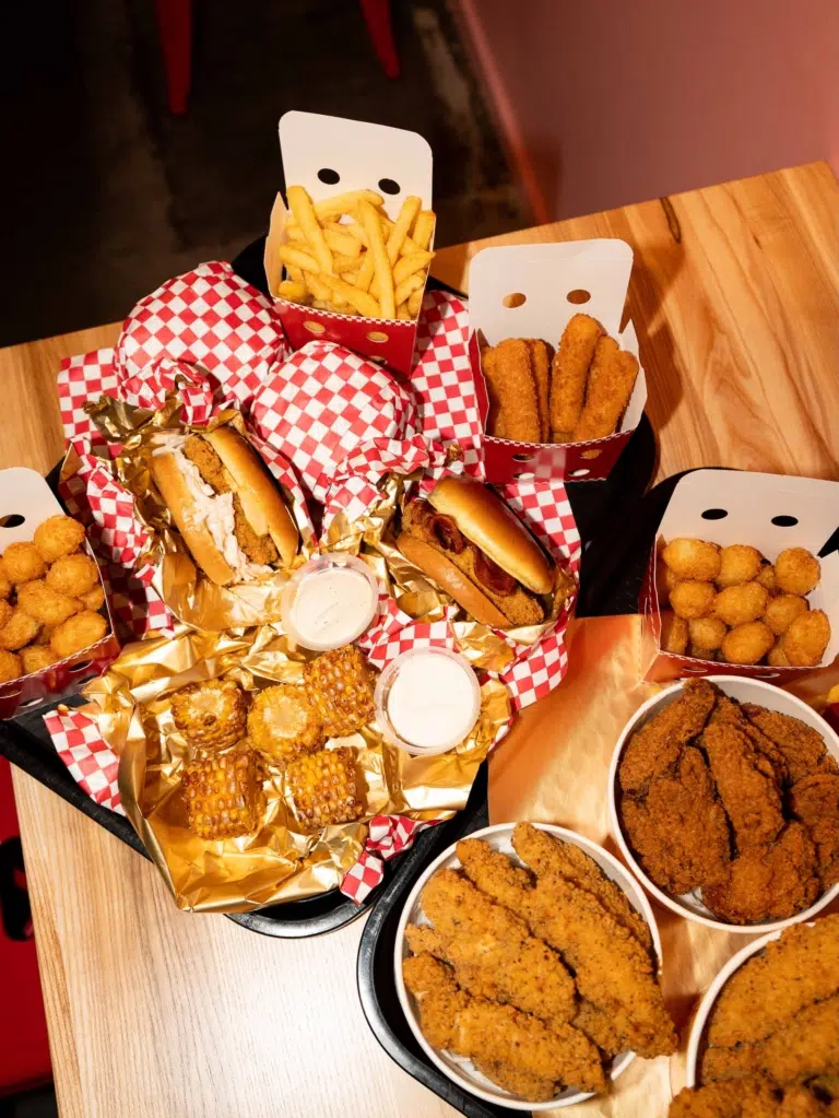 Chicken-Burger, panierte Hühnerstücke, Pommes und weitere Beilagen auf einem Tisch bei Loco Chicken.