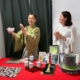 Koshi Hagimura hält eine Teeschale neben Rie Kuroki; vor ihnen stehen Matcha-Dosen, Teegeschirr und eine Steinmühle.