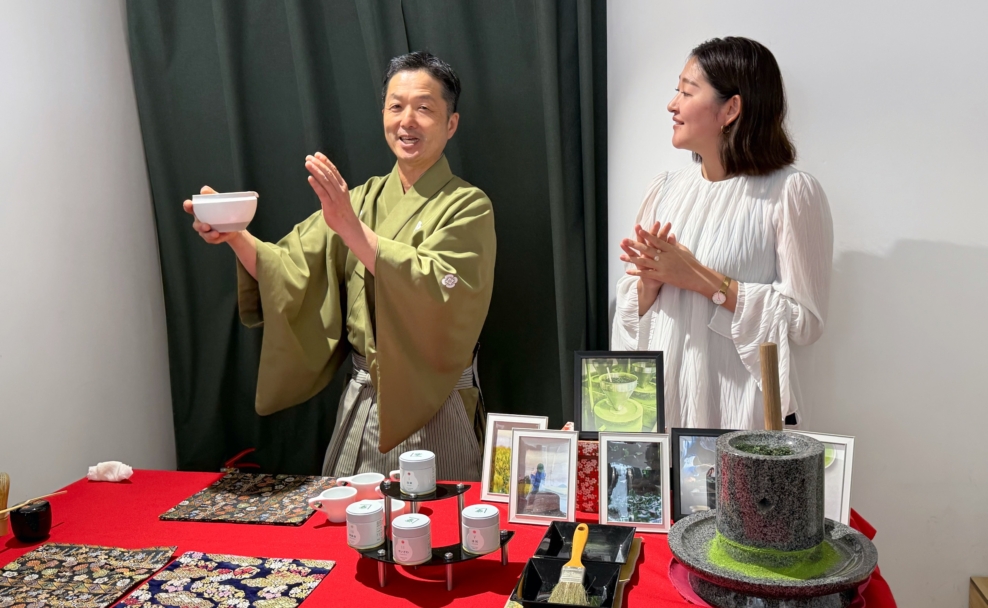 Koshi Hagimura hält eine Teeschale neben Rie Kuroki; vor ihnen stehen Matcha-Dosen, Teegeschirr und eine Steinmühle.