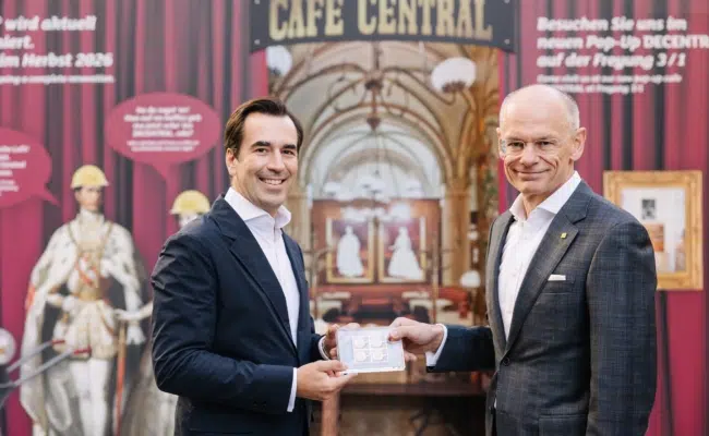 Martin Winkler und Walter Oblin zeigen die Jubiläumsbriefmarke vor dem mit einer Abbildung gestalteten Eingang des Café Central.